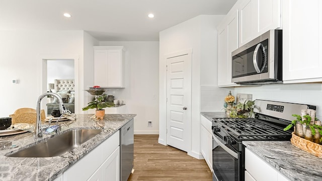 kitchen with light stone countertops, sink, stainless steel appliances, light hardwood / wood-style flooring, and white cabinets