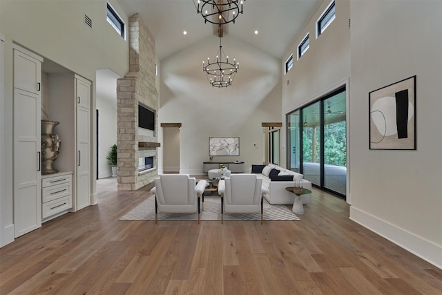 living room featuring a fireplace, high vaulted ceiling, a chandelier, and light hardwood / wood-style flooring