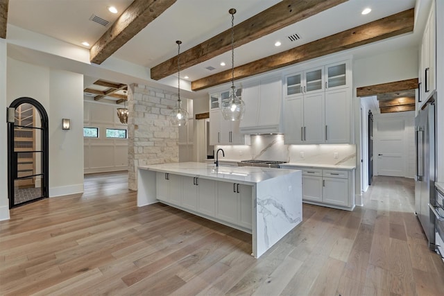 kitchen with hanging light fixtures, light stone countertops, light wood-type flooring, beam ceiling, and white cabinetry