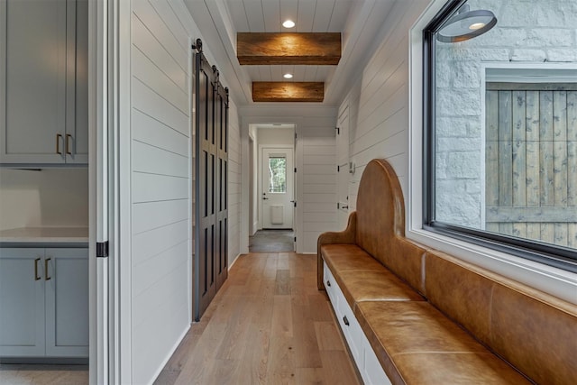 hall with beamed ceiling, light wood-type flooring, and a barn door