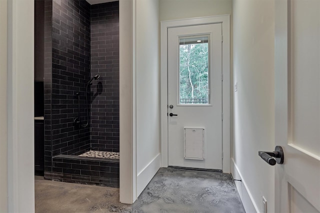 bathroom with tiled shower and concrete floors