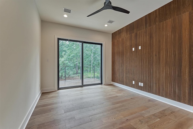 unfurnished room with ceiling fan, light hardwood / wood-style floors, and wooden walls