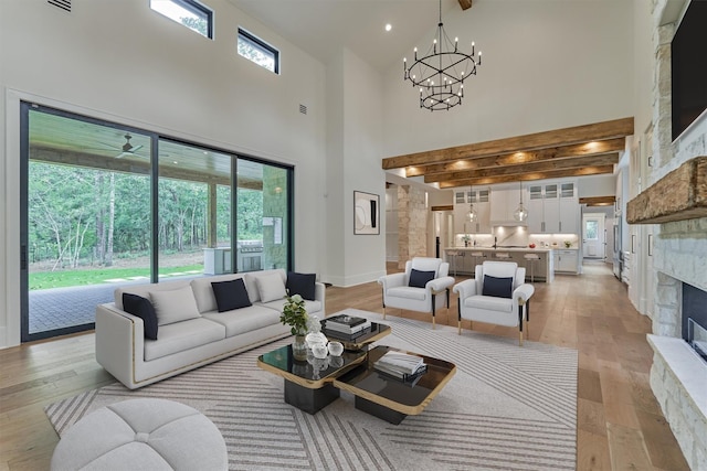 living room with a stone fireplace, light hardwood / wood-style flooring, a towering ceiling, and ceiling fan with notable chandelier