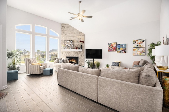 living room featuring a stone fireplace, ceiling fan, light hardwood / wood-style flooring, and high vaulted ceiling