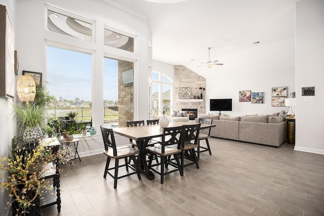 dining area with a stone fireplace, ceiling fan, hardwood / wood-style floors, and high vaulted ceiling