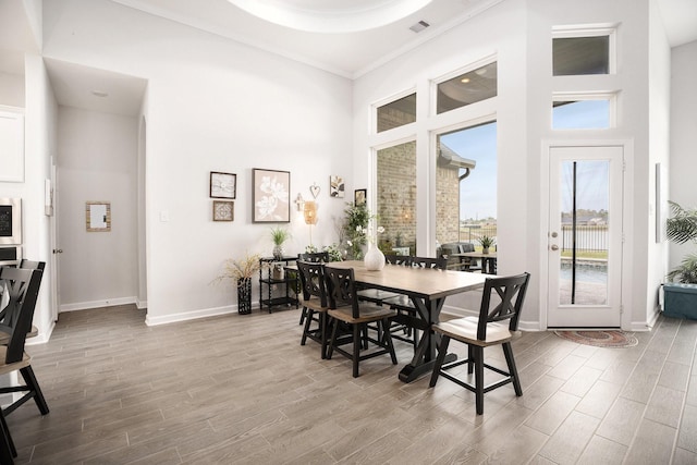 dining space with a high ceiling, light wood-type flooring, and ornamental molding