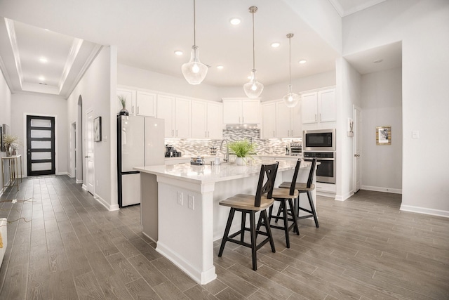 kitchen featuring stainless steel appliances, decorative light fixtures, a center island with sink, white cabinets, and hardwood / wood-style flooring