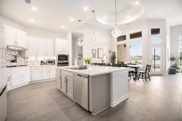 kitchen with white cabinets, hardwood / wood-style floors, stainless steel appliances, and a center island with sink