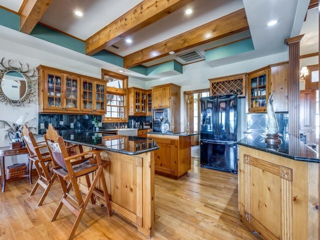 kitchen with tasteful backsplash, black fridge, decorative columns, a kitchen island, and a breakfast bar area