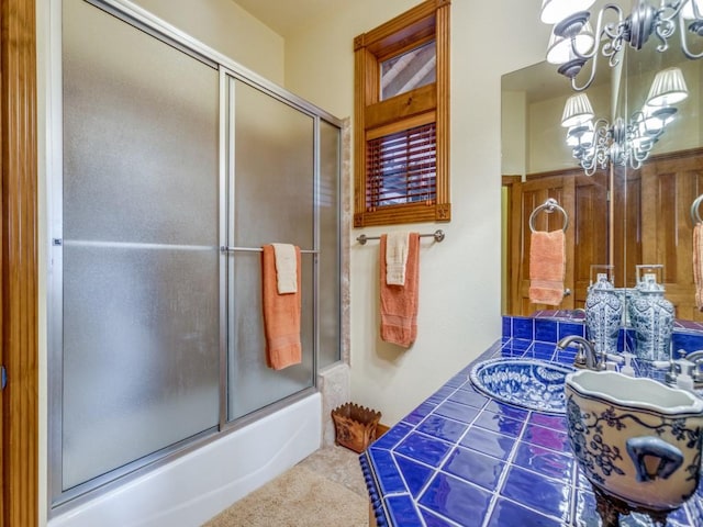 bathroom with sink, a notable chandelier, and combined bath / shower with glass door