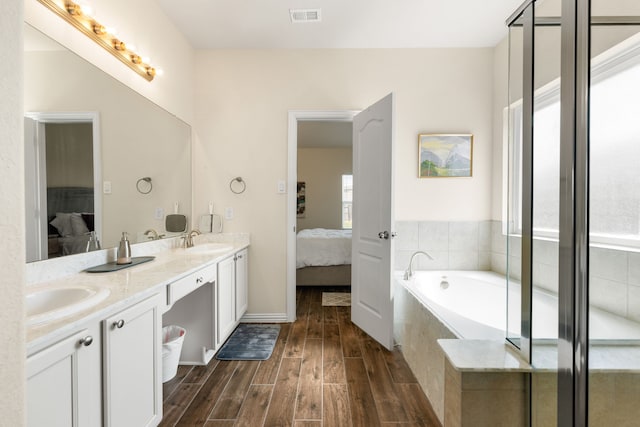 bathroom featuring hardwood / wood-style floors, a relaxing tiled tub, and vanity