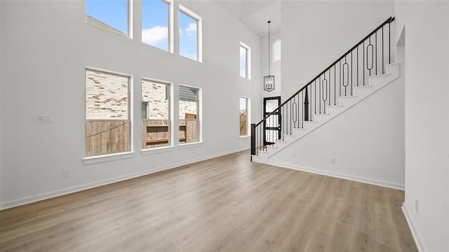 unfurnished living room featuring a high ceiling, light hardwood / wood-style flooring, and a notable chandelier