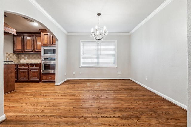 kitchen with backsplash, a chandelier, wood-type flooring, appliances with stainless steel finishes, and ornamental molding