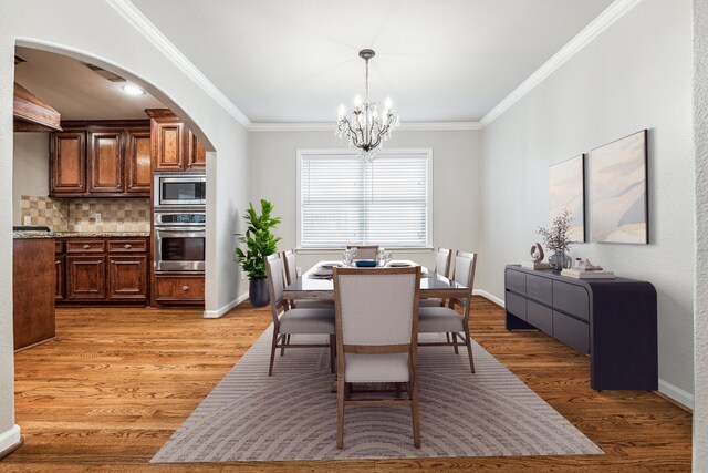 dining space featuring light wood-type flooring, ornamental molding, and a chandelier