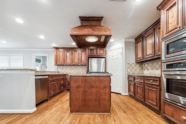 kitchen with appliances with stainless steel finishes, light wood-type flooring, light stone counters, ornamental molding, and a center island