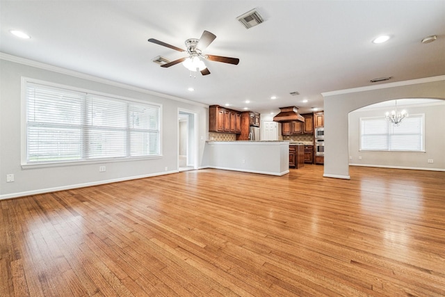 unfurnished living room with crown molding, plenty of natural light, ceiling fan with notable chandelier, and light wood-type flooring