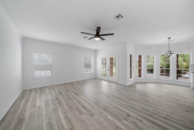 unfurnished living room featuring french doors, a healthy amount of sunlight, ceiling fan with notable chandelier, and light hardwood / wood-style floors