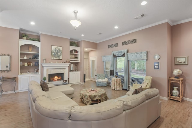 living room featuring a tiled fireplace, crown molding, and light hardwood / wood-style flooring