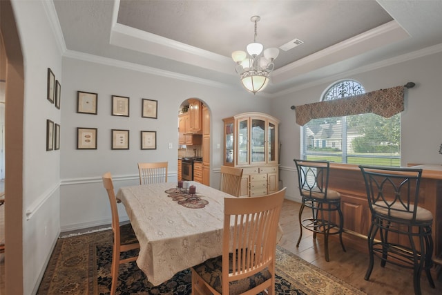 dining area with a raised ceiling, crown molding, a notable chandelier, and hardwood / wood-style flooring