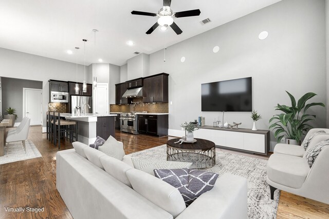 living room featuring a towering ceiling, ceiling fan, and dark wood-type flooring