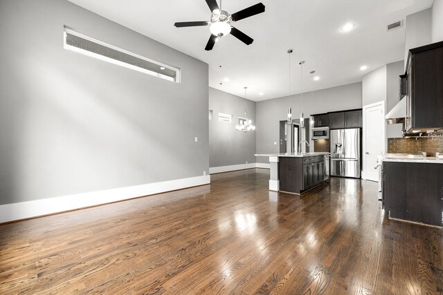 kitchen with a high ceiling, a center island with sink, ceiling fan with notable chandelier, hanging light fixtures, and stainless steel appliances