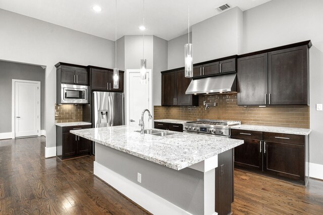 kitchen featuring a kitchen island with sink, sink, light stone counters, dark brown cabinetry, and stainless steel appliances