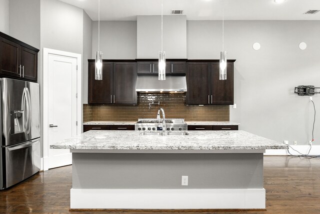 kitchen with stainless steel refrigerator with ice dispenser, dark brown cabinetry, a center island with sink, and decorative light fixtures