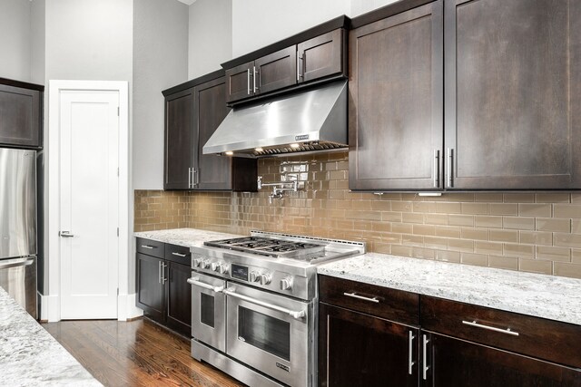 kitchen featuring dark wood-type flooring, decorative backsplash, light stone countertops, appliances with stainless steel finishes, and dark brown cabinetry