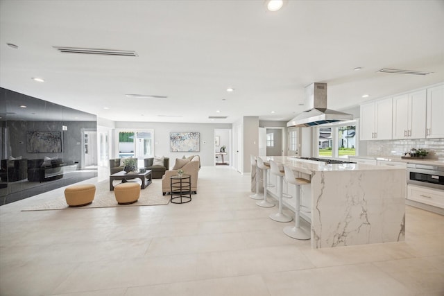 kitchen with a breakfast bar area, island exhaust hood, white cabinetry, and plenty of natural light