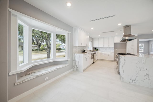 kitchen with decorative backsplash, appliances with stainless steel finishes, light stone countertops, island range hood, and white cabinets