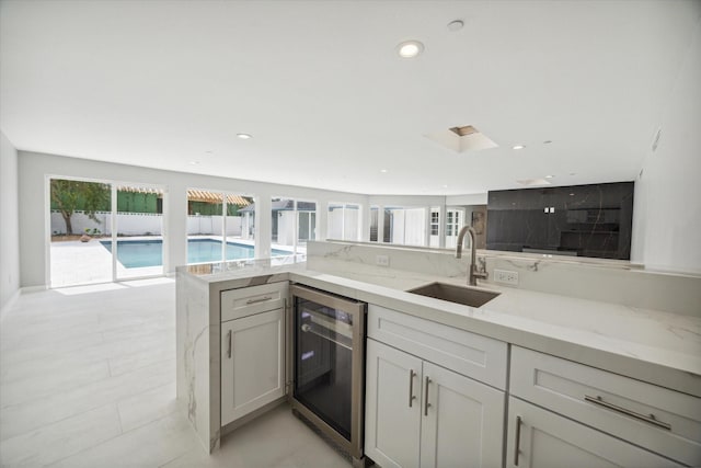 kitchen with sink, light tile patterned floors, light stone counters, kitchen peninsula, and beverage cooler