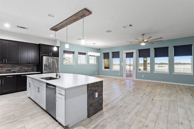 kitchen with tasteful backsplash, ceiling fan with notable chandelier, stainless steel appliances, a kitchen island with sink, and hanging light fixtures