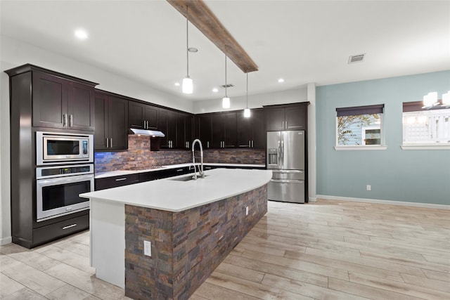 kitchen with appliances with stainless steel finishes, light wood-type flooring, dark brown cabinetry, and a kitchen island with sink