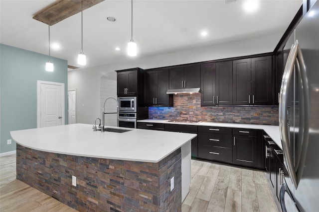 kitchen with a center island with sink, sink, light hardwood / wood-style flooring, decorative light fixtures, and stainless steel appliances