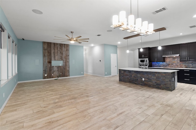 kitchen with pendant lighting, backsplash, an island with sink, and light hardwood / wood-style flooring