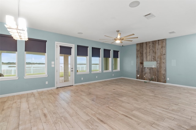 unfurnished living room with a water view, ceiling fan with notable chandelier, and light wood-type flooring