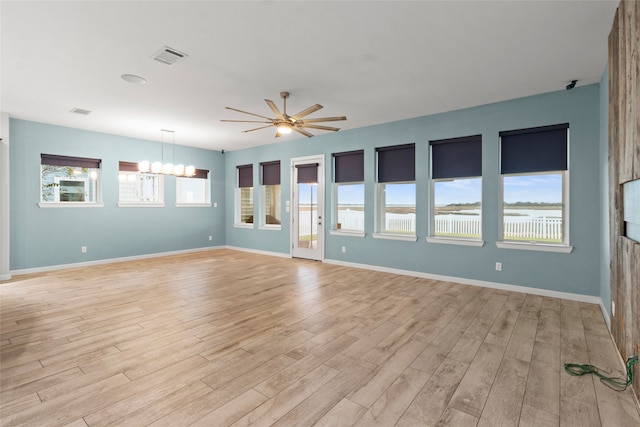 empty room featuring ceiling fan with notable chandelier, light wood-type flooring, and a wealth of natural light