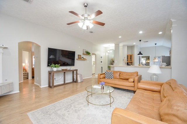 living room featuring a textured ceiling, light wood-type flooring, vaulted ceiling, and ceiling fan