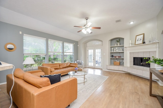 living room featuring lofted ceiling, french doors, ceiling fan, light wood-type flooring, and a tiled fireplace