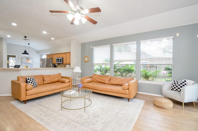 living room featuring a wealth of natural light, ceiling fan, vaulted ceiling, and light wood-type flooring