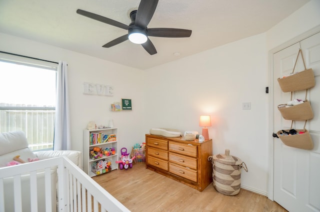 bedroom featuring ceiling fan, light hardwood / wood-style flooring, and a nursery area