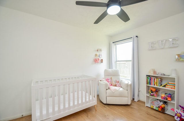 bedroom featuring ceiling fan, hardwood / wood-style floors, and a nursery area