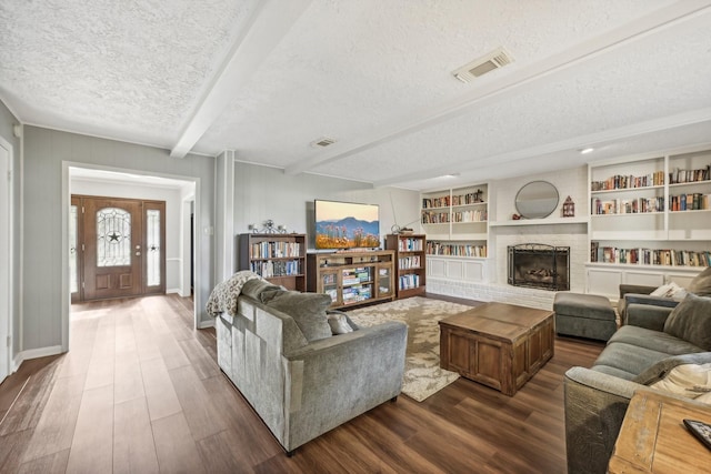 living room featuring beam ceiling, dark hardwood / wood-style flooring, a textured ceiling, and a brick fireplace