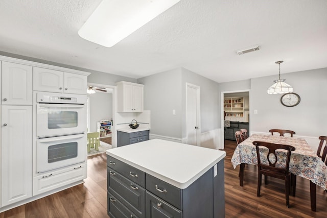 kitchen with white double oven, hanging light fixtures, a kitchen island, dark hardwood / wood-style flooring, and white cabinetry