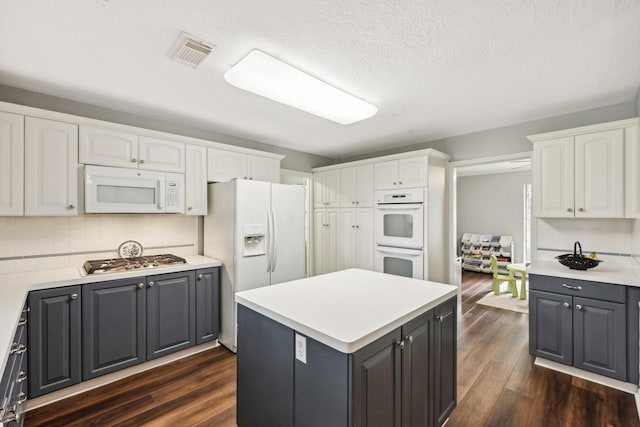 kitchen featuring white appliances, decorative backsplash, a textured ceiling, dark hardwood / wood-style flooring, and white cabinetry