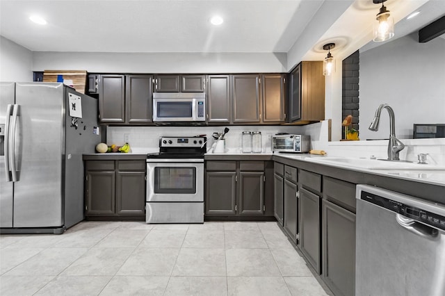 kitchen with appliances with stainless steel finishes, dark brown cabinets, sink, light tile patterned floors, and hanging light fixtures