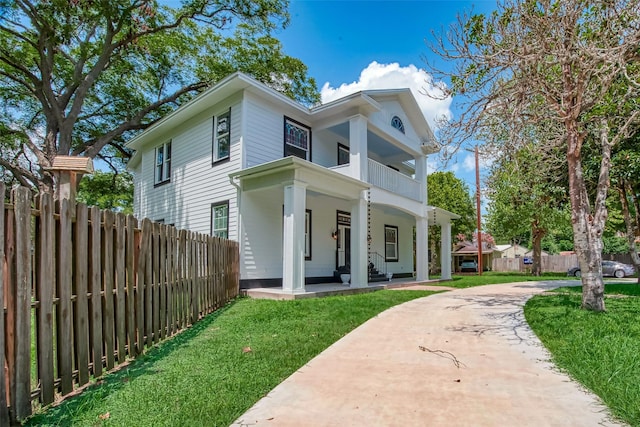 greek revival house featuring a porch, a balcony, and a front yard