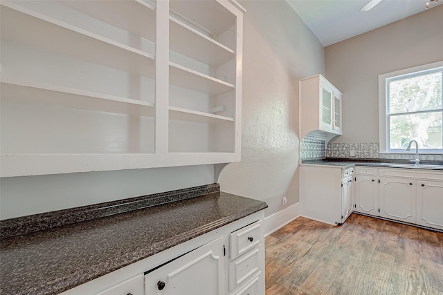 kitchen with light wood-type flooring, white cabinetry, sink, and dark stone counters