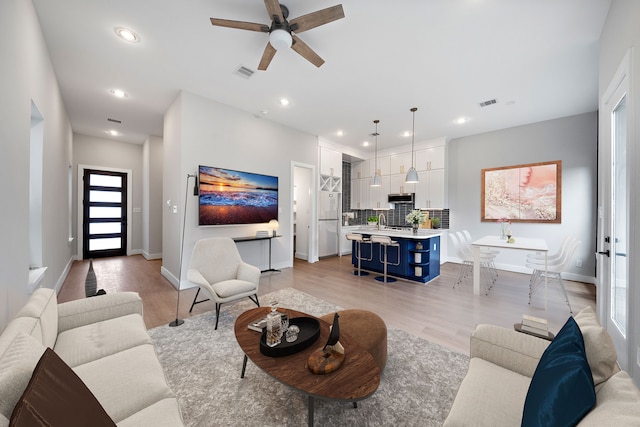 living room featuring sink, light hardwood / wood-style floors, and ceiling fan