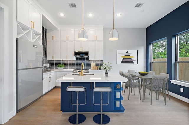 kitchen with a breakfast bar, white cabinetry, an island with sink, hanging light fixtures, and fridge